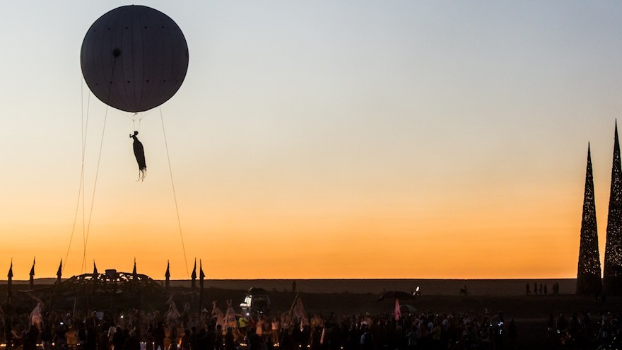 A hot air balloon lifts an acrobat into the sky.