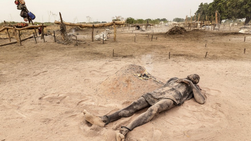 A Mundari man relaxes in the soft, peach-coloured ash and dust of a dung fire. Image: © Tariq Zaidi / ZUMA Press