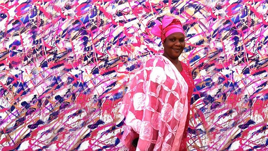 A woman stands in front of a mural by street artist Tanc in the Medina neighbourhood of Dakar.