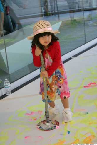 A child uses a giant stamp dipped in paint to create a large floor mural. 