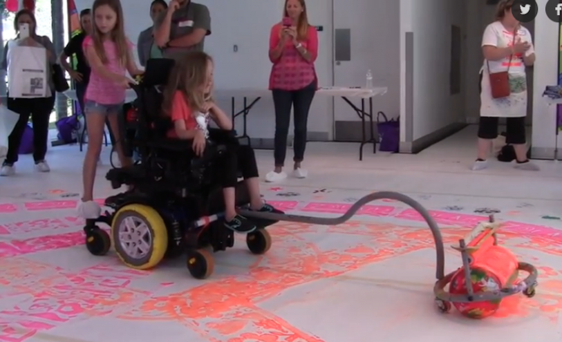 A giant paint roller is fixed to the wheelchair and allows children to  create giant paintings by rolling on their wheelchairs.