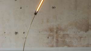 This brass and walnut wood lamp sways gently, mimicking a blade of grass in the wind. 