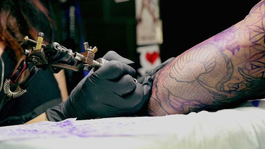 Manuela works on Roger's tattoo.