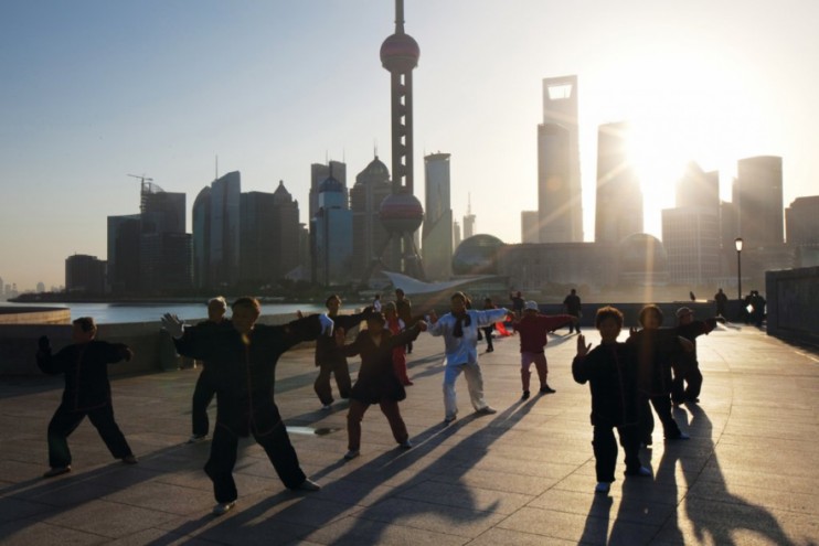 Elderly people practicing Tai Chi Chuan on the Bund as the sun rises over the sk
