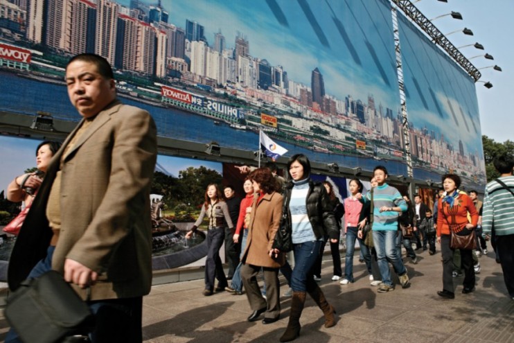 Tourists and passers-by walk pass a giant urban planning billboard on Nanjing Ea